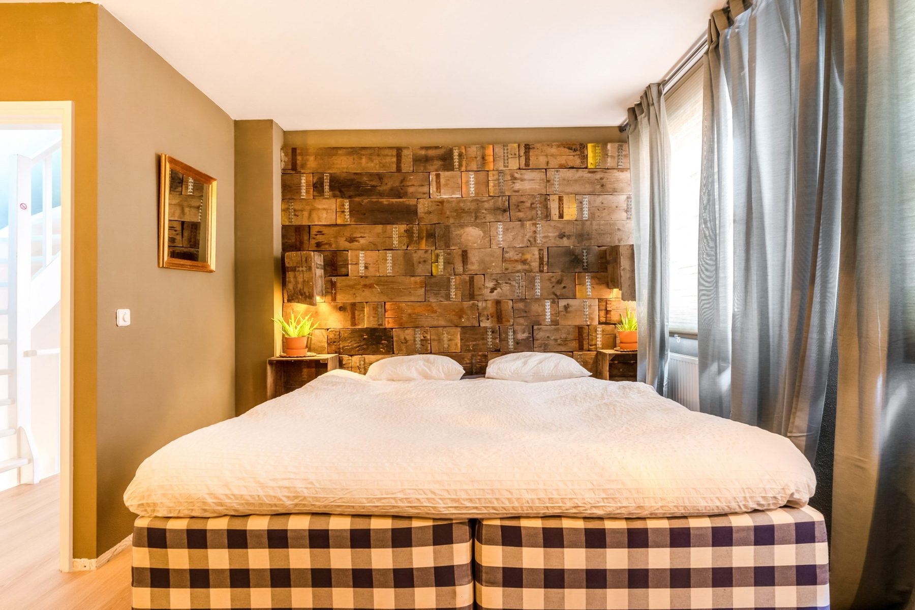 Slaapkamer met tweepersoonsbed tegen een houten wand