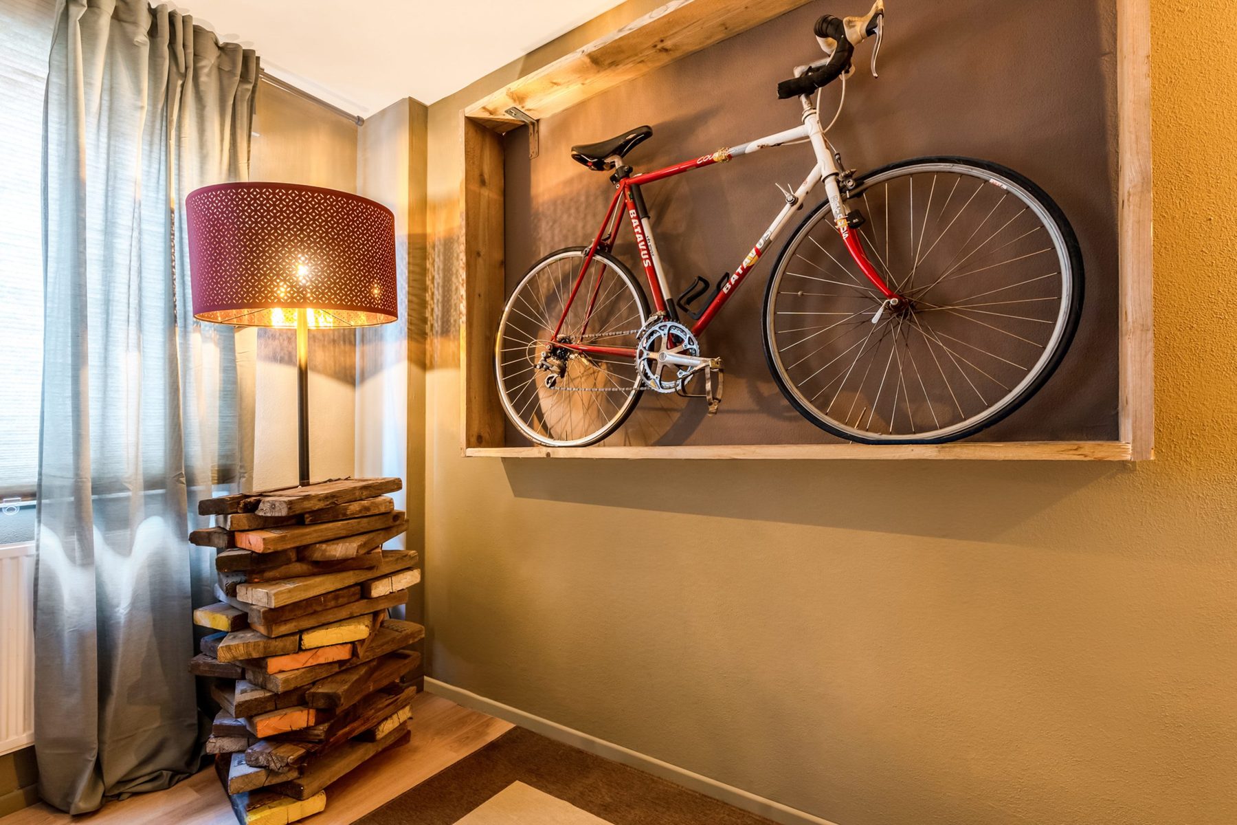 Racefiets aan de muur boven een houten kastje met schemerlamp